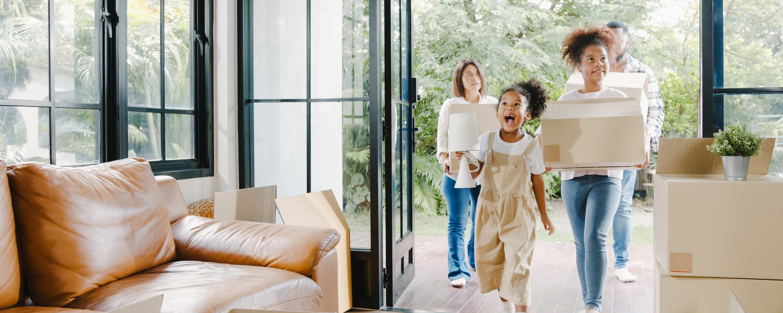 Happy African American young family bought new house. Mom, Dad, and child smiling happy hold cardboard boxes for move object walking into big modern home. New real estate dwelling, loan and mortgage.